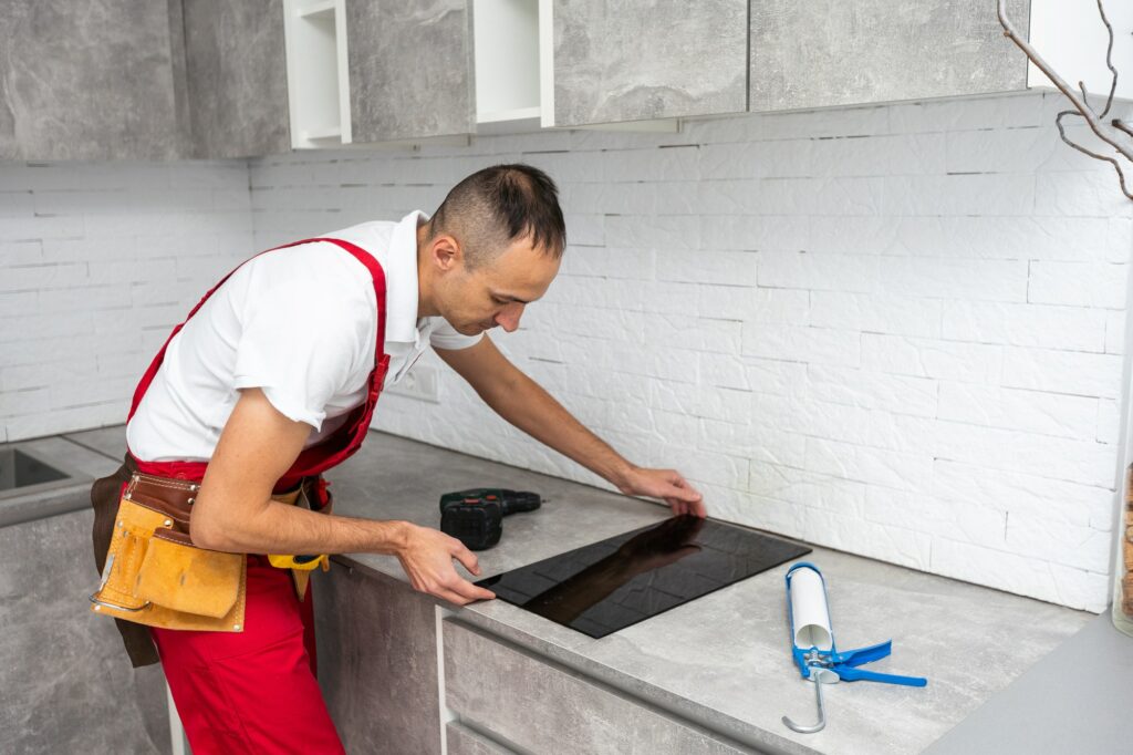 Young Repairman Installing Induction Cooker In Kitchen