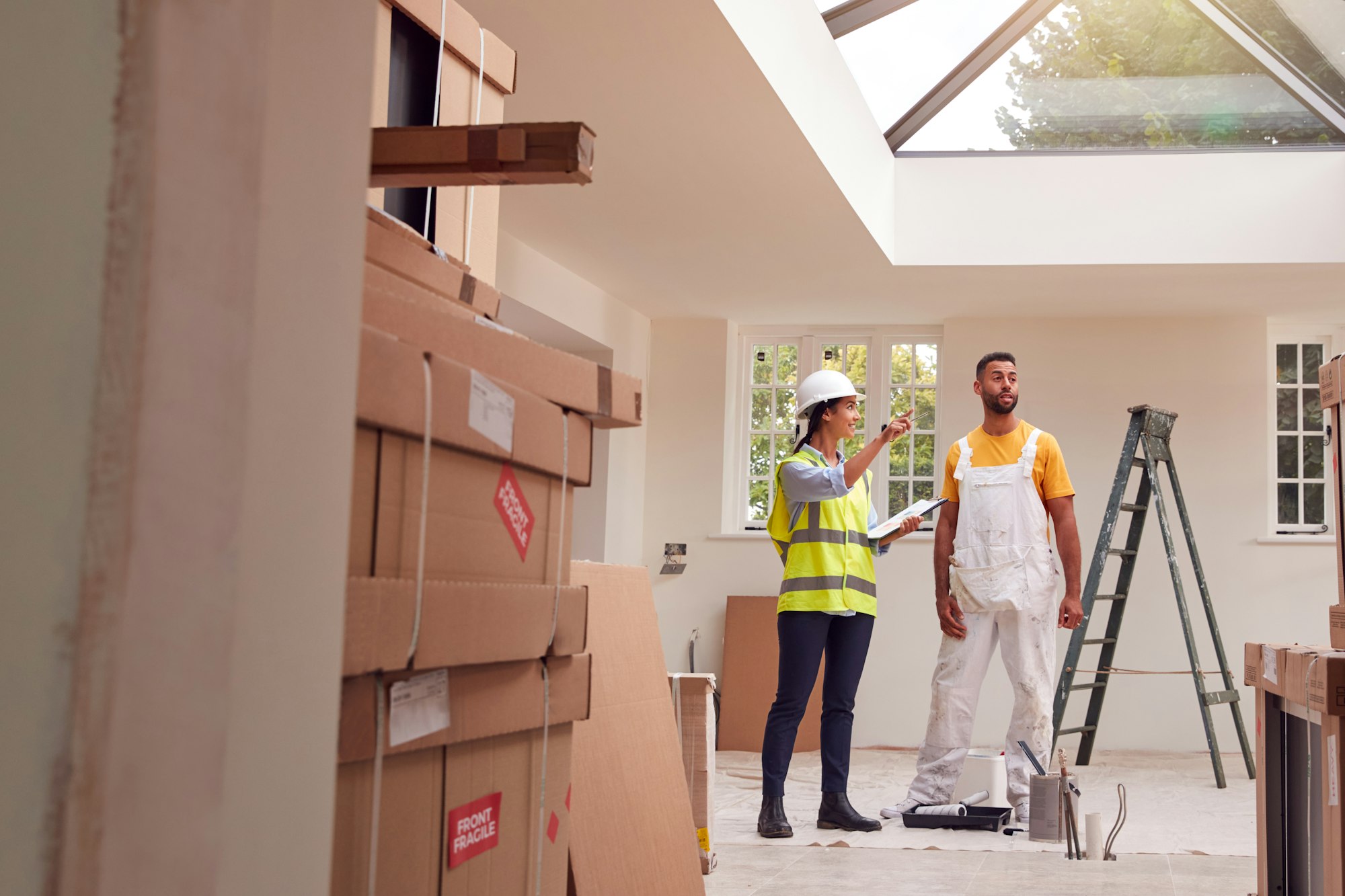 Female Surveyor With Clipboard Meeting With Decorator Working Inside Property