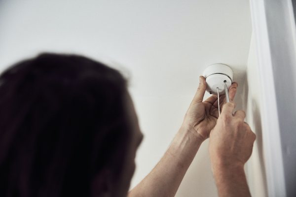 An electrician screwing the cap on a light fitting on the ceiling.