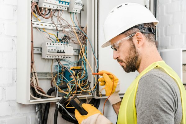 handsome electrician checking electrical box with multimetr in corridor