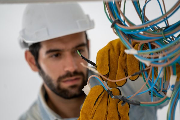 Professional electrician installing cables in wires of new house at construction site.